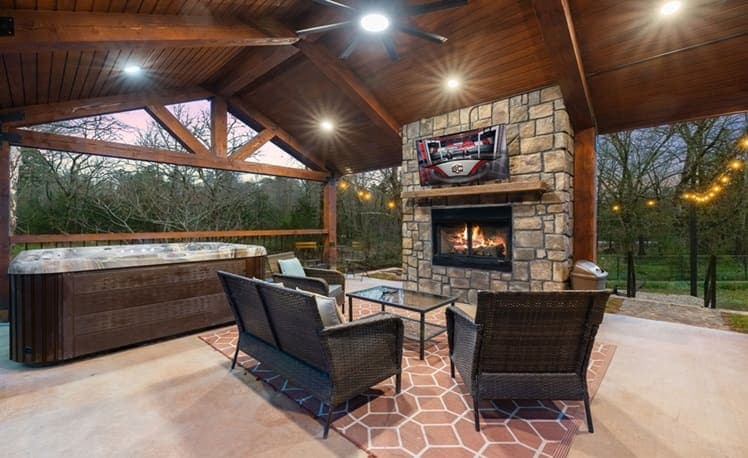 Hot tub on the covered creek-side porch with outdoor fireplace and TV