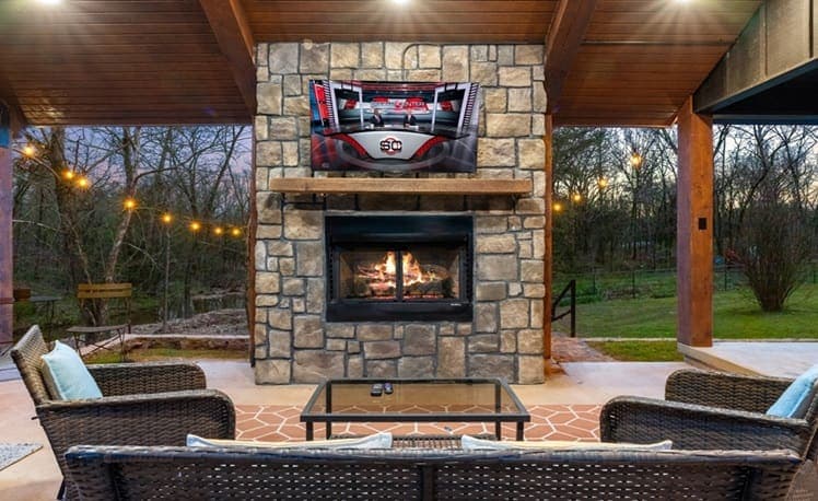 Outdoor fireplace with TV, seating, and string lights on the porch